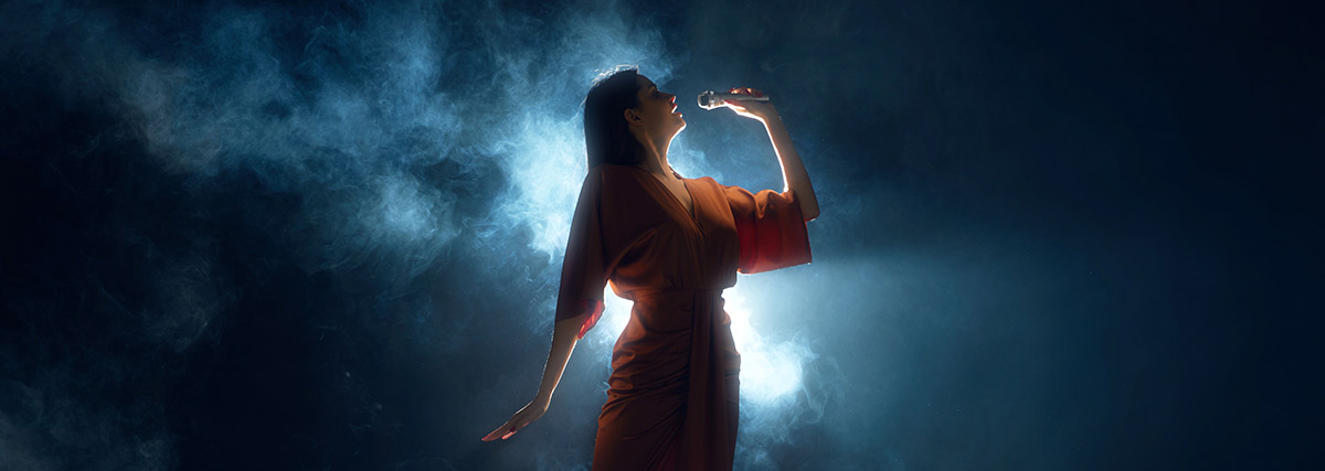 Woman in dress singing on stage against black background